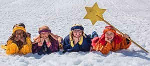 4 Kinder liegen als Dreikönige verkleidet im Schnee und lächeln.